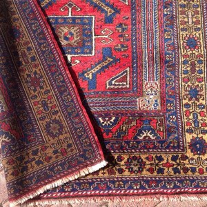 May include: A red, blue, and gold patterned rug with a fringed edge. The rug has a traditional design with intricate details.