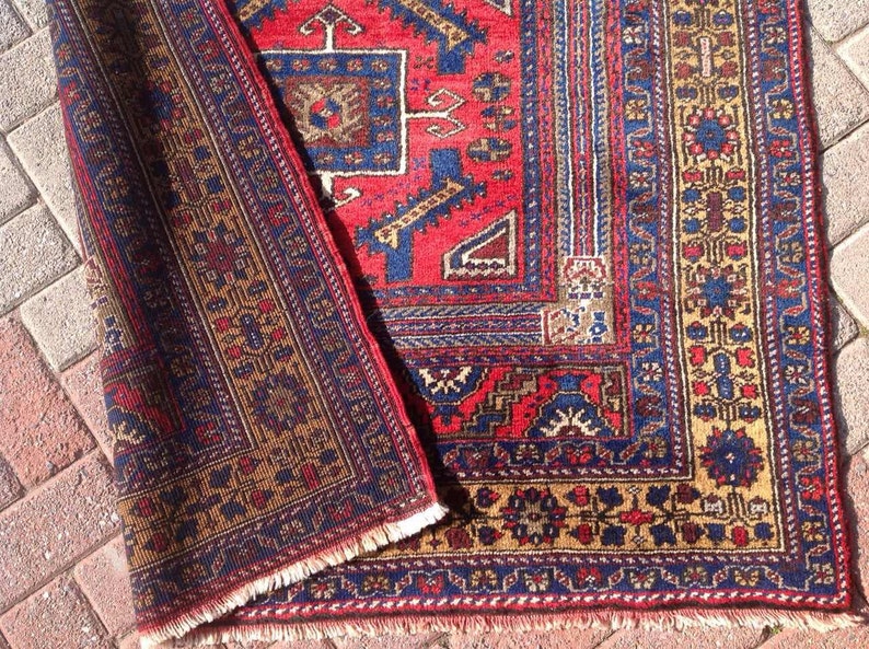 May include: A red, blue, and gold patterned rug with a fringed edge. The rug has a traditional design with intricate details.