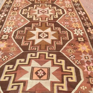 Puede incluir: Una alfombra turca tradicional con un patr&oacute;n geom&eacute;trico marr&oacute;n, beige y rosa. La alfombra presenta un dise&ntilde;o repetitivo de estrellas y cuadrados.