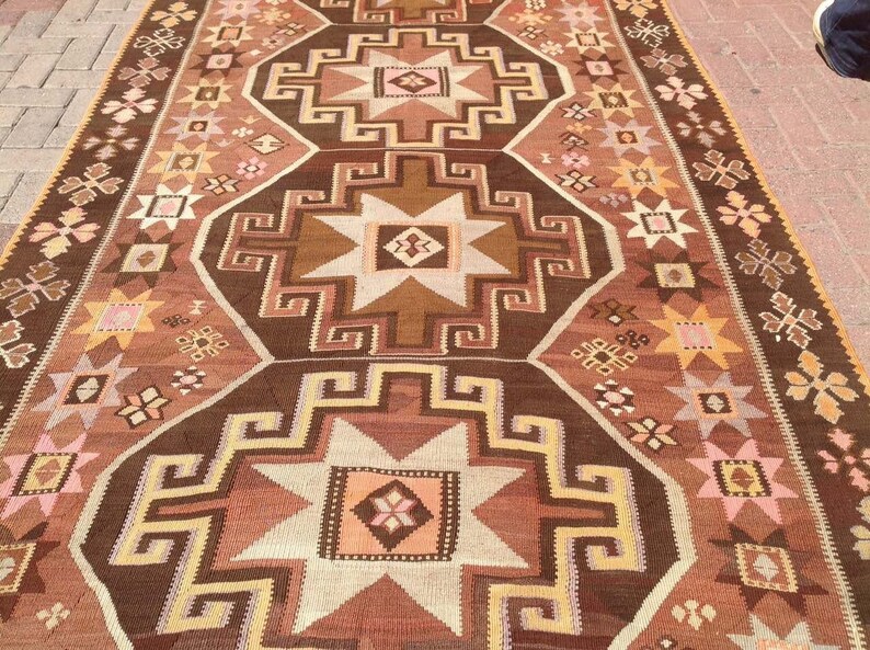 Puede incluir: Una alfombra turca tradicional con un patr&oacute;n geom&eacute;trico marr&oacute;n, beige y rosa. La alfombra presenta un dise&ntilde;o repetitivo de estrellas y cuadrados.