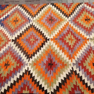 May include: A colorful rug with a geometric pattern in shades of orange, red, purple, brown, and white. The rug has a diamond-shaped design with a central starburst motif.