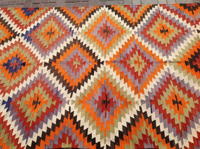 May include: A colorful rug with a geometric pattern in shades of orange, red, purple, brown, and white. The rug has a diamond-shaped design with a central starburst motif.