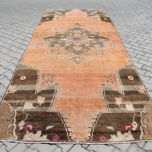 May include: An orange and brown vintage rug with a central medallion design. The rug features a distressed look with faded colors and intricate patterns. The rug's border is a darker brown, and the central design includes shades of brown, tan, and pink.