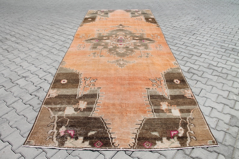 May include: An orange and brown vintage rug with a central medallion design. The rug features a distressed look with faded colors and intricate patterns. The rug's border is a darker brown, and the central design includes shades of brown, tan, and pink.