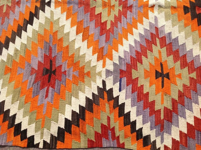 May include: A colorful rug with a geometric pattern in shades of orange, red, purple, brown, and white.