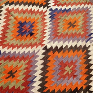 May include: A colorful rug with a geometric pattern in shades of orange, red, brown, white, and purple.