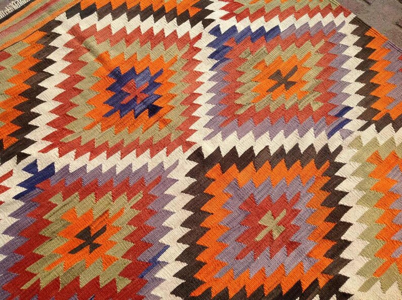 May include: A colorful rug with a geometric pattern in shades of orange, red, brown, white, and purple.
