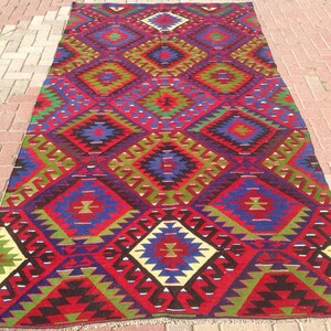 May include: A traditional Turkish rug with a geometric pattern in shades of red, blue, green, and white. The rug has a diamond-shaped design with intricate details.