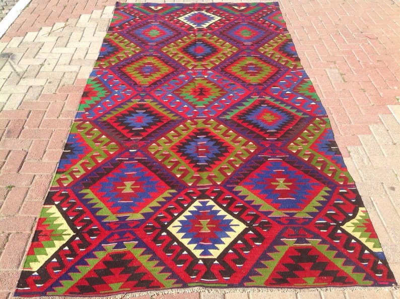 May include: A traditional Turkish rug with a geometric pattern in shades of red, blue, green, and white. The rug has a diamond-shaped design with intricate details.