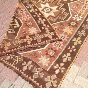 Puede incluir: Una alfombra de color marr&oacute;n y beige con flecos. La alfombra tiene un dise&ntilde;o geom&eacute;trico con estrellas y flores.