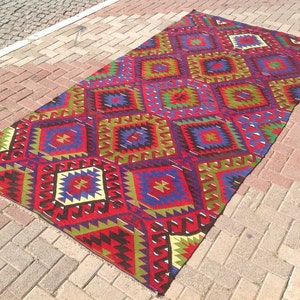 May include: A colorful, geometric patterned rug with a red, green, blue, and yellow color scheme. The rug is made of wool and has a traditional design.