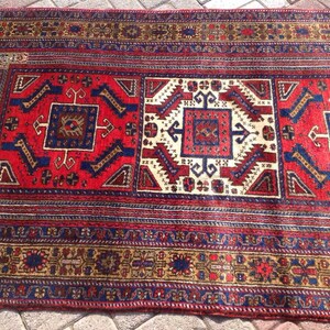 May include: A red, blue, and cream colored rug with a traditional geometric pattern. The rug has a fringe border.