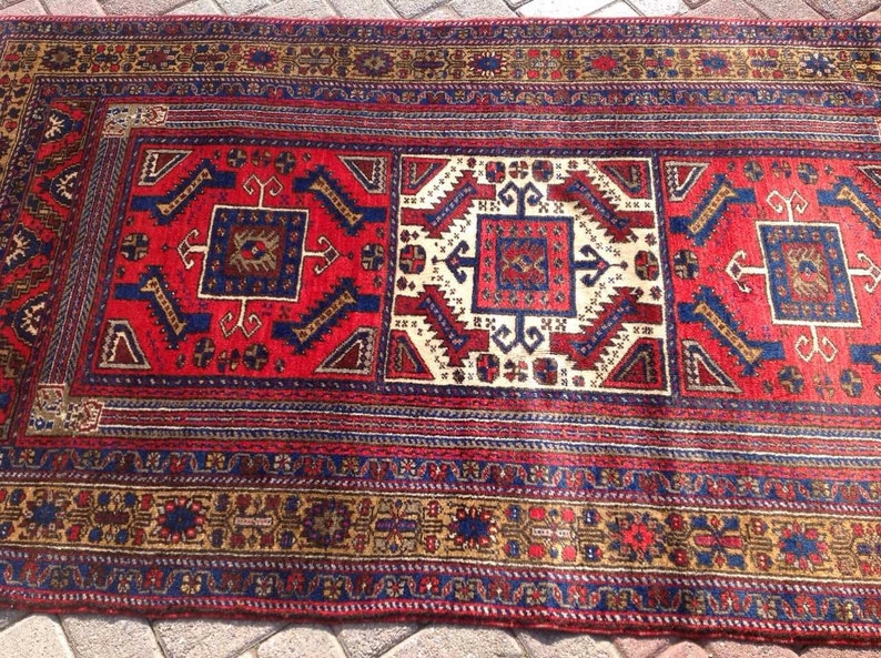 May include: A red, blue, and cream colored rug with a traditional geometric pattern. The rug has a fringe border.