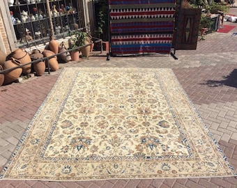 Puede incluir: Una alfombra rectangular grande con un intrincado diseño floral en tonos crema, azul y marrón. La alfombra presenta un borde detallado y se exhibe al aire libre sobre una superficie de ladrillo. La alfombra es de estilo tradicional.