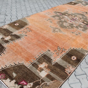 May include: An orange and brown vintage rug with a central medallion design. The rug features geometric patterns in shades of brown, beige, and pink. The rug is rectangular and appears to be made of woven material.