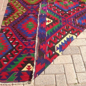 May include: A colorful, hand-woven rug with a geometric pattern in shades of red, blue, green, and black. The rug has a fringed edge and is folded in half.
