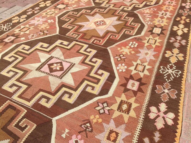 Puede incluir: Una alfombra turca tradicional con un patr&oacute;n geom&eacute;trico marr&oacute;n, beige y rosa. La alfombra presenta un dise&ntilde;o de estrella central rodeado de estrellas m&aacute;s peque&ntilde;as y motivos florales.
