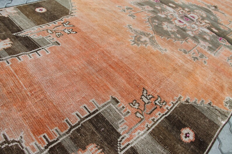 May include: An antique, distressed rug with a warm color palette. The rug features a central field of faded orange, bordered by geometric patterns in shades of brown, gray, and beige. The design includes floral and geometric motifs.