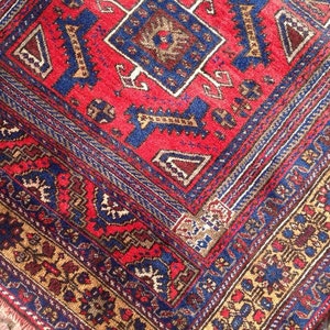 May include: A red, blue, and gold patterned rug with intricate designs. The rug has a central diamond shape with smaller geometric patterns surrounding it.