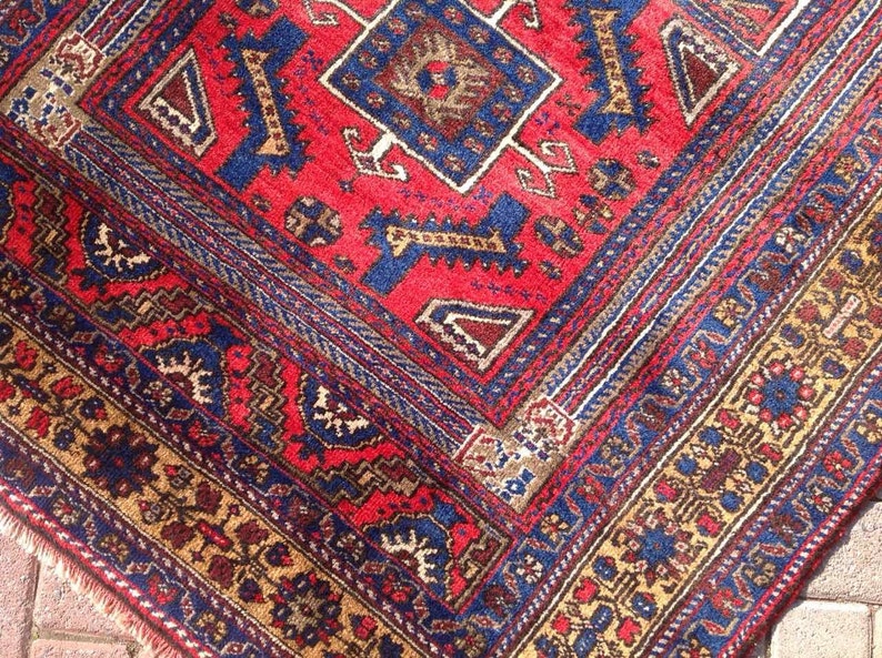 May include: A red, blue, and gold patterned rug with intricate designs. The rug has a central diamond shape with smaller geometric patterns surrounding it.