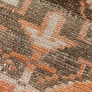 May include: Close-up of a textured rug with a geometric pattern. The rug features a repeating design in shades of brown, orange, and cream. The fibers are tightly woven, creating a dense, durable surface. The rug's design is a blend of modern and traditional styles.