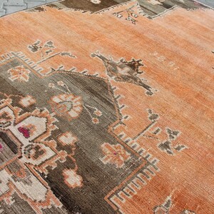 May include: An orange and brown vintage rug with a geometric and floral pattern. The rug has a distressed look with faded colors and a detailed border. The rug is rectangular and appears to be made of woven material.