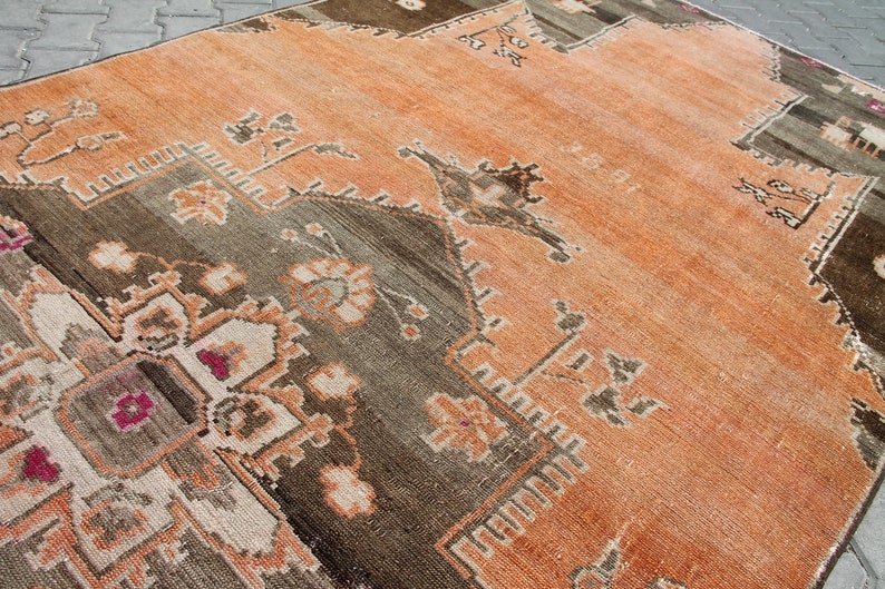 May include: An orange and brown vintage rug with a geometric and floral pattern. The rug has a distressed look with faded colors and a detailed border. The rug is rectangular and appears to be made of woven material.