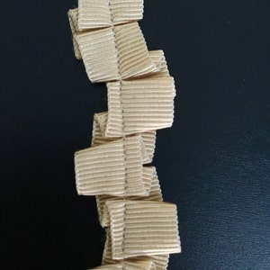 May include: A beige ruffled trim with a textured surface. The trim is folded and stacked, creating a vertical pattern.