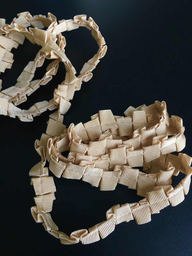 May include: A close-up of a beige ruffled trim. The trim is made of a soft, pliable material and has a delicate, feminine look.