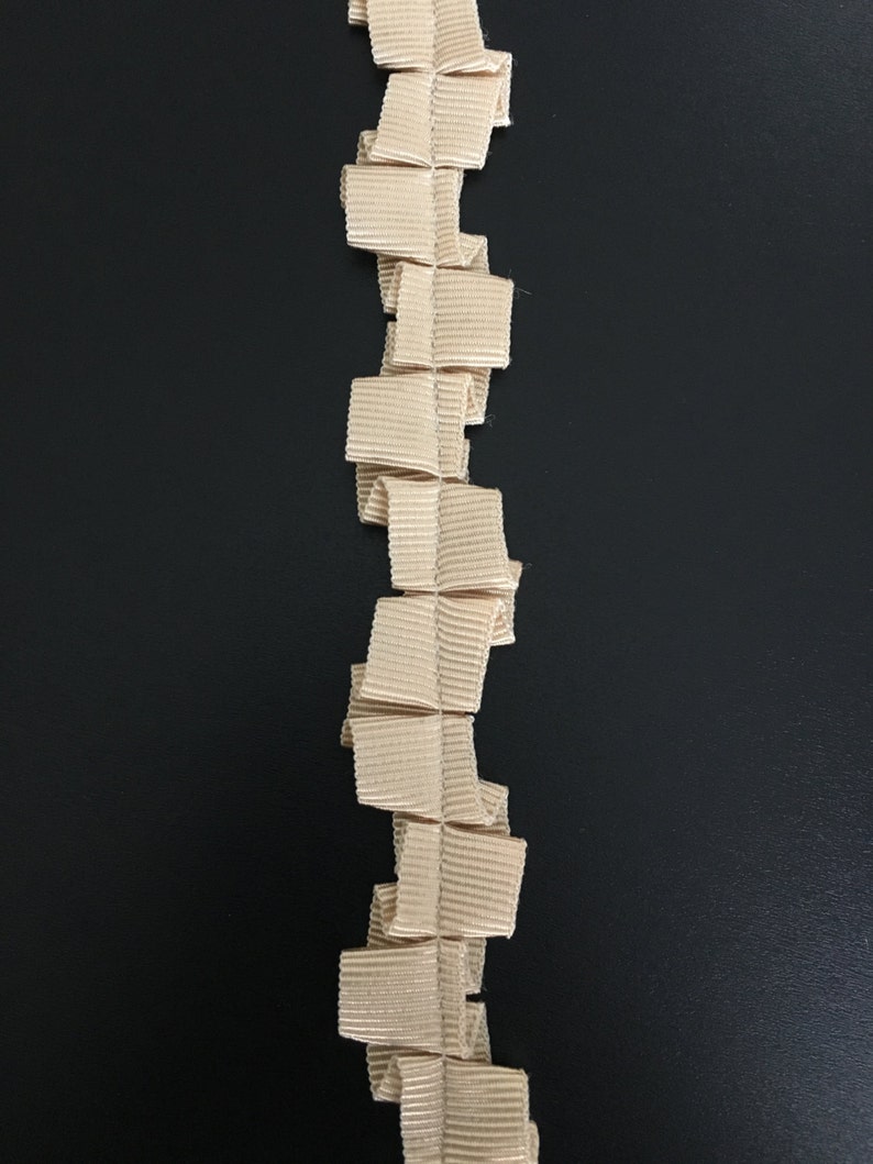 May include: A beige ruffled trim with a textured surface. The trim is made of a soft, pliable material and is perfect for adding a touch of elegance to any project.
