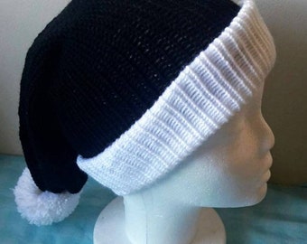 May include: A black knit hat with a white brim and a white pom-pom. The hat is displayed on a white mannequin head. The hat's design is a classic winter style.