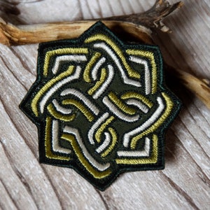 Könnte beinhalten: Ein gestickter Aufnäher mit einem keltischen Knotendesign in Grün, Weiß und Gold.