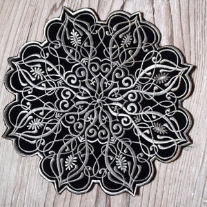 May include: Black and white embroidered patch with a detailed floral and scroll design. The patch has a scalloped edge and a symmetrical, circular pattern. The embroidery is in white thread on a black background.
