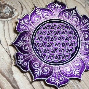 Könnte beinhalten: Lilafarbener gestickter Patch mit einem Blumendesign und einem silberfarbenen geometrischen Muster in der Mitte.