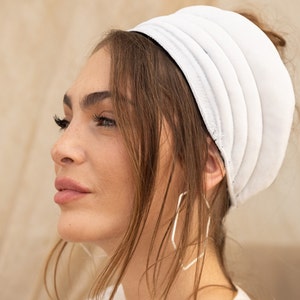 Puede incluir: Una diadema blanca con diseño plisado. La diadema la lleva puesta una persona con el pelo largo y castaño.