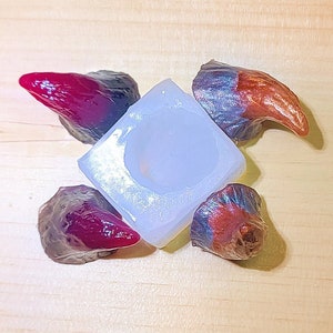 May include: A silicone mold for making devil horn shapes. The mold is white and has four impressions of devil horns. Two of the horns are red and two are brown.