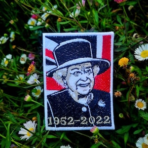 May include: A white embroidered patch featuring a black and white image of Queen Elizabeth II wearing a black hat and a white collar. The patch has a red, white and blue Union Jack flag in the background and the text "1952-2022" in gold lettering.