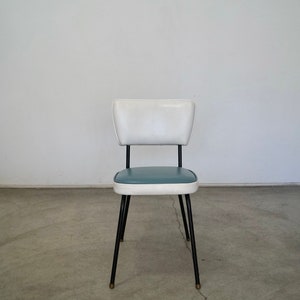 May include: A retro-style chair with a white backrest and a teal seat. The chair has a black metal frame and legs. The seat is trimmed with white. The chair is a vintage piece, likely from the mid-century modern era.