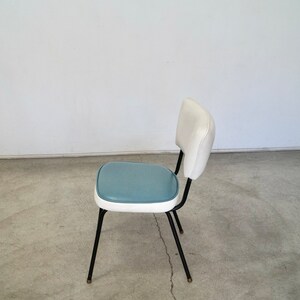May include: A retro-style chair with a white back and a teal seat. The chair has a black metal frame and legs. The seat and back are upholstered. The chair is a vintage piece, perfect for a kitchen or dining room.