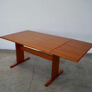 May include: A rectangular wooden table with a light brown finish. The table has a central support and two legs. The table's top is split into two sections, with one section extended. The table is approximately 60 inches long.
