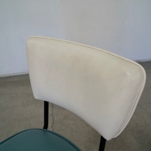 May include: A mid-century modern chair with a white, curved backrest and a teal seat. The chair has black metal legs and a minimalist design, suitable for a dining room or office space.