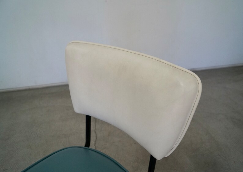 May include: A mid-century modern chair with a white, curved backrest and a teal seat. The chair has black metal legs and a minimalist design, suitable for a dining room or office space.