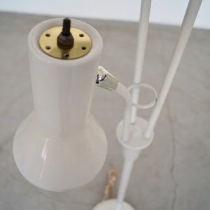 May include: A white, mid-century modern style floor lamp. The lamp features a rounded shade, a brass-colored top, and a slender, curved arm. The lamp's base and supporting structure are white.