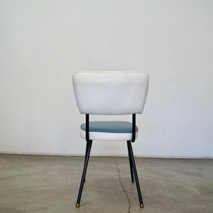 May include: A mid-century modern chair with a white backrest and a blue seat. The chair has black metal legs with brass-colored tips. The chair is approximately 30 inches tall.