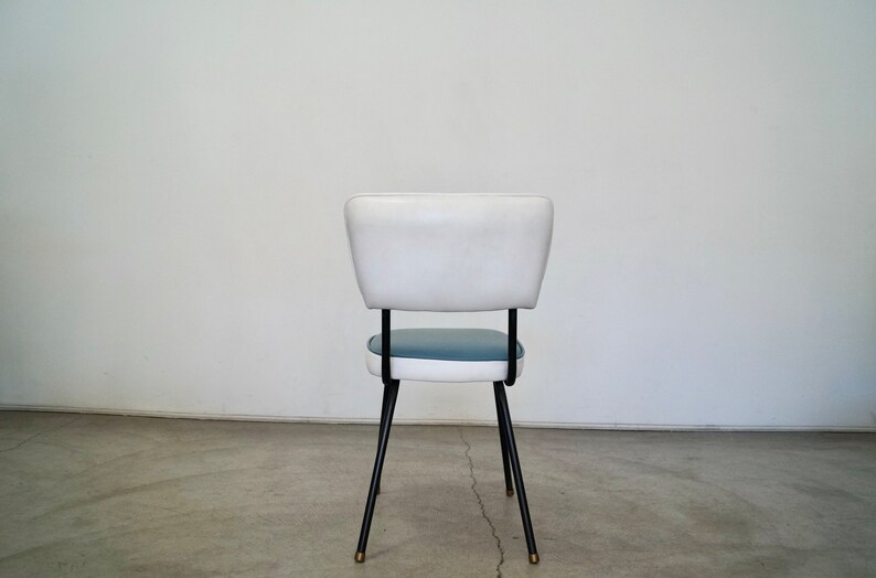 May include: A mid-century modern chair with a white backrest and a blue seat. The chair has black metal legs with brass-colored tips. The chair is approximately 30 inches tall.