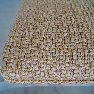 May include: Close-up of a woven cushion with a textured surface. The cushion is made of natural-colored fibers, creating a neutral, earthy tone. The weave pattern is visible, adding to the tactile quality of the design. The cushion appears to be part of a chair or stool.
