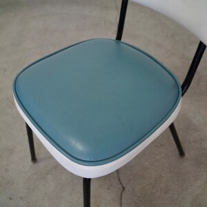 May include: A retro-style chair with a blue seat and white backrest. The seat is square with rounded corners and a white trim. The chair has black metal legs and a curved back support. The design is reminiscent of mid-century modern furniture.