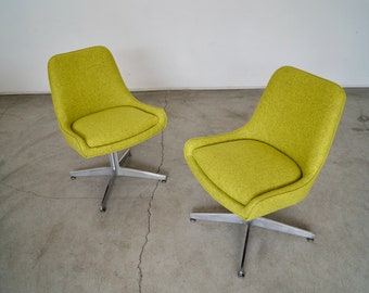 May include: Two mid-century modern swivel chairs. The chairs have a bright green textured fabric seat and back. The base is made of silver metal with a five-star design. The chairs are on a concrete floor.