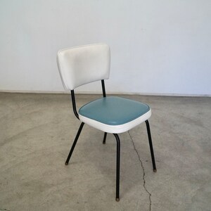 May include: A retro-style chair with a white backrest and a teal seat, outlined in white. The chair has black metal legs with brass-colored tips. The chair is a vintage piece, perfect for a kitchen or dining room.