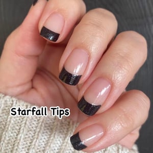 May include: Close-up of a hand with black glitter tipped nails. The tips are a black glitter polish with a clear base. The text "Starfall Tips" is visible in the image.